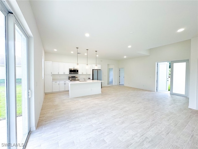 kitchen featuring stainless steel appliances, white cabinets, hanging light fixtures, an island with sink, and light wood-type flooring