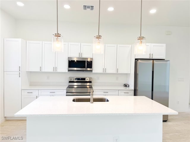 kitchen with light hardwood / wood-style floors, stainless steel appliances, white cabinets, a kitchen island with sink, and pendant lighting