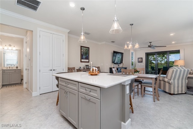 kitchen featuring a kitchen island, a kitchen breakfast bar, pendant lighting, gray cabinets, and ornamental molding