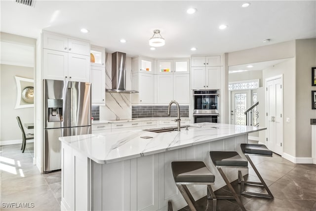 kitchen featuring sink, stainless steel appliances, a center island with sink, and wall chimney range hood