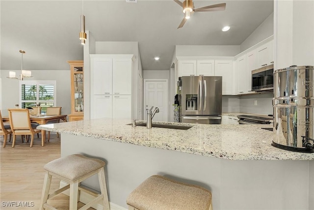 kitchen with kitchen peninsula, appliances with stainless steel finishes, sink, pendant lighting, and white cabinetry