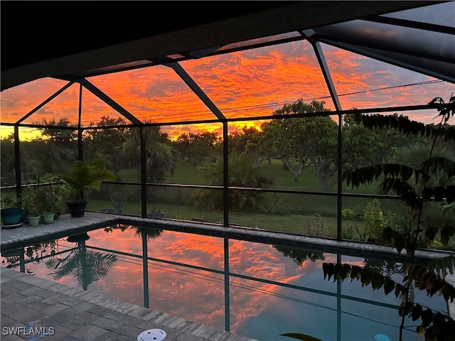 pool at dusk featuring glass enclosure and a patio