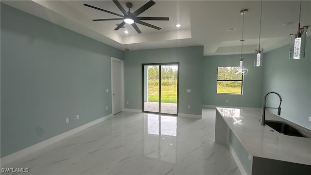 interior space featuring sink, decorative light fixtures, a raised ceiling, light stone counters, and ceiling fan