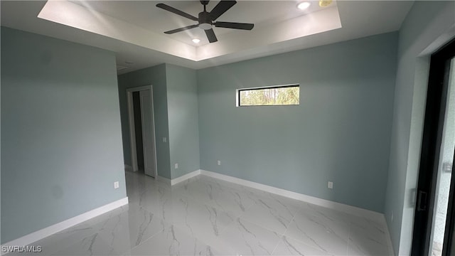 empty room with ceiling fan and a raised ceiling