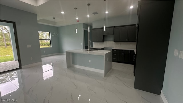 kitchen featuring sink, a kitchen island with sink, pendant lighting, and tasteful backsplash