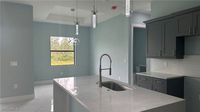 kitchen with a center island with sink, decorative light fixtures, sink, and light stone counters