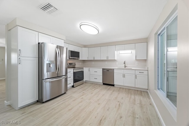 kitchen featuring stainless steel appliances, light hardwood / wood-style floors, sink, and white cabinets