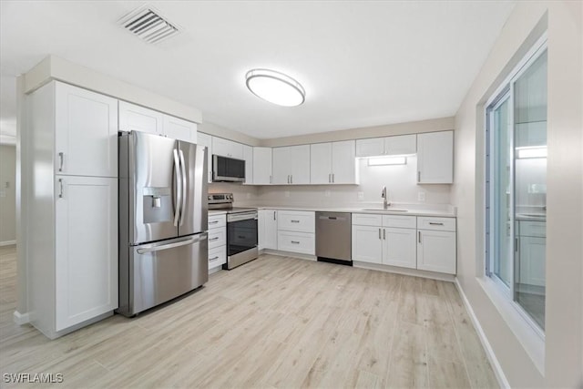 kitchen with stainless steel appliances, a sink, visible vents, light countertops, and light wood-type flooring