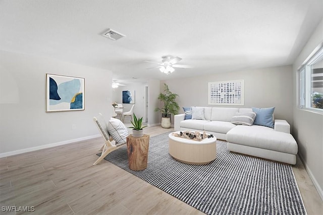 living area with ceiling fan, light wood-style flooring, visible vents, and baseboards