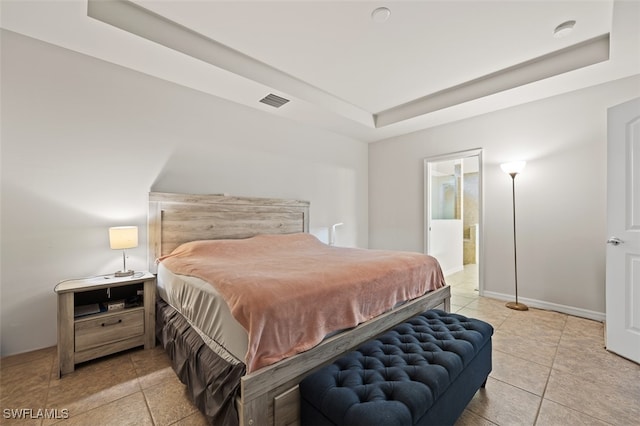 bedroom featuring light tile patterned flooring, a tray ceiling, and ensuite bath