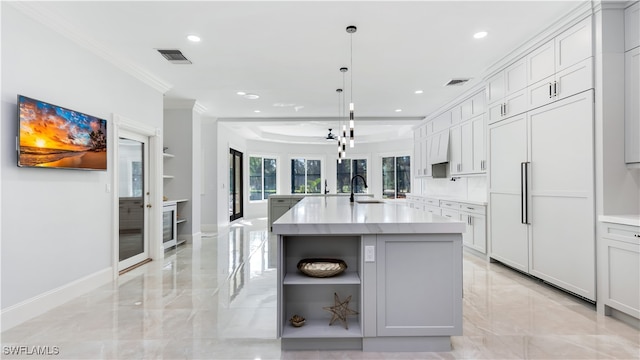 kitchen with a kitchen island with sink, paneled refrigerator, ornamental molding, sink, and pendant lighting