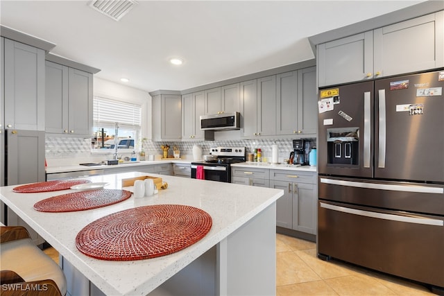 kitchen featuring a center island, a kitchen bar, light tile patterned flooring, gray cabinets, and appliances with stainless steel finishes