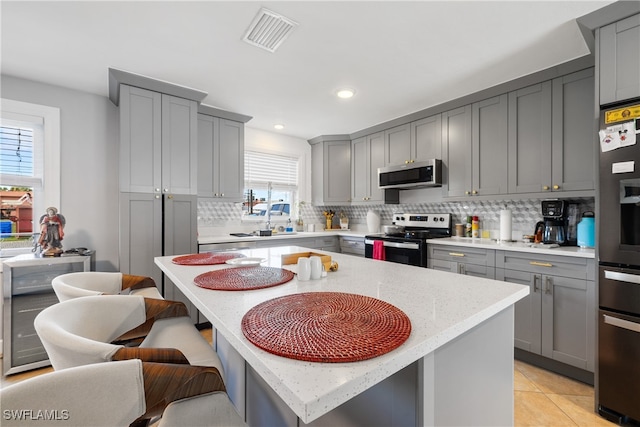 kitchen featuring appliances with stainless steel finishes, a wealth of natural light, a kitchen island, and gray cabinets