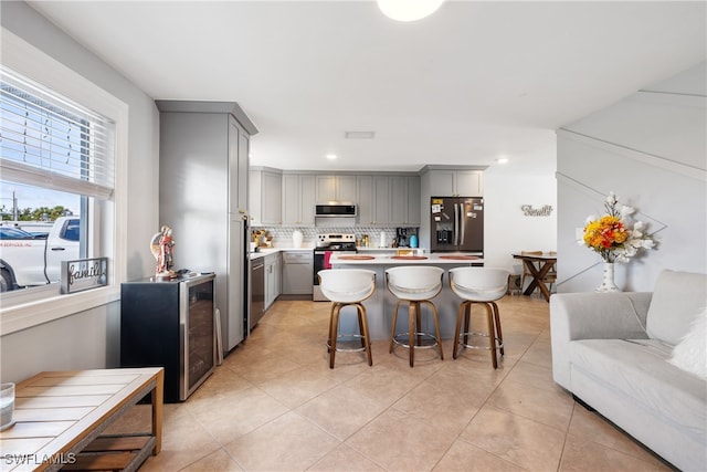 kitchen featuring gray cabinetry, appliances with stainless steel finishes, a kitchen bar, a kitchen island, and backsplash