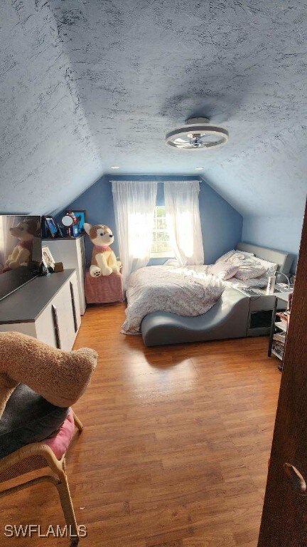 bedroom featuring vaulted ceiling, a textured ceiling, and light hardwood / wood-style flooring