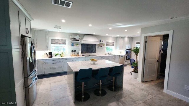 kitchen featuring a breakfast bar area, appliances with stainless steel finishes, premium range hood, a kitchen island, and light stone counters