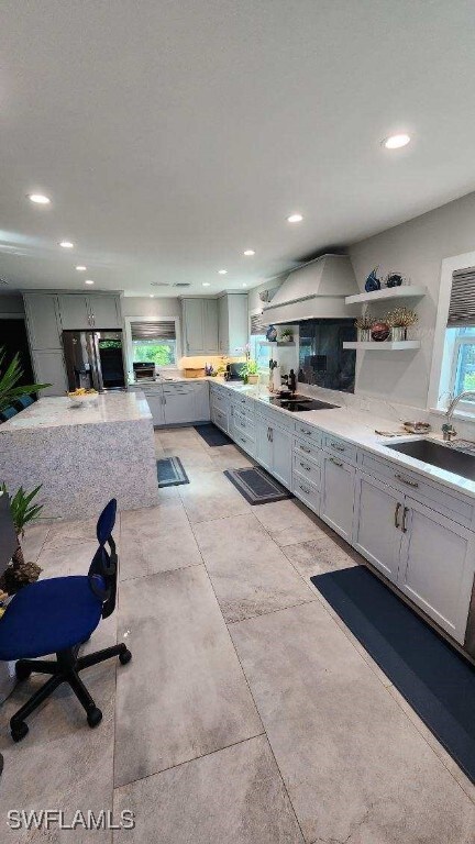 kitchen featuring light stone countertops, sink, fridge, black electric cooktop, and premium range hood