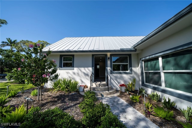 doorway to property featuring a standing seam roof, metal roof, and stucco siding