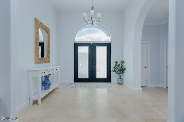 tiled foyer entrance featuring a towering ceiling, a notable chandelier, crown molding, and french doors