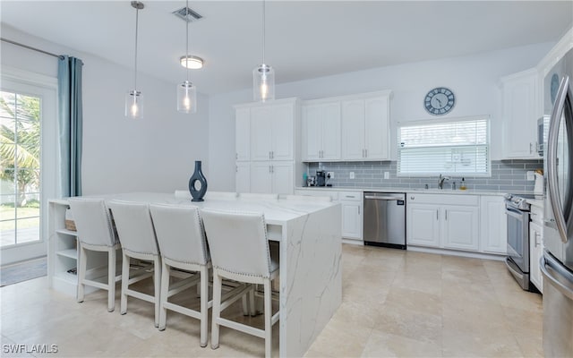 kitchen with appliances with stainless steel finishes, tasteful backsplash, a kitchen island, white cabinetry, and hanging light fixtures