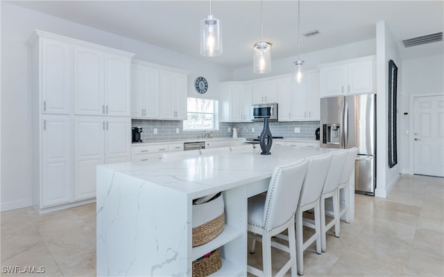 kitchen with light stone countertops, a center island, hanging light fixtures, stainless steel appliances, and white cabinets