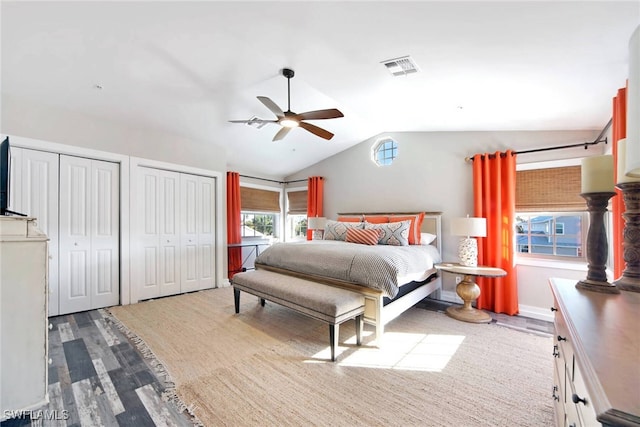 bedroom with ceiling fan, multiple closets, light wood-type flooring, and vaulted ceiling