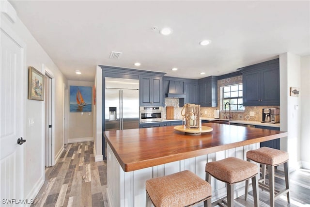 kitchen with premium range hood, blue cabinets, sink, light hardwood / wood-style floors, and stainless steel appliances