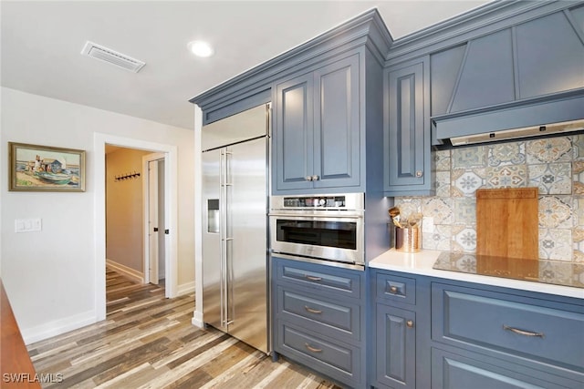 kitchen with hardwood / wood-style floors, blue cabinetry, tasteful backsplash, custom range hood, and stainless steel appliances