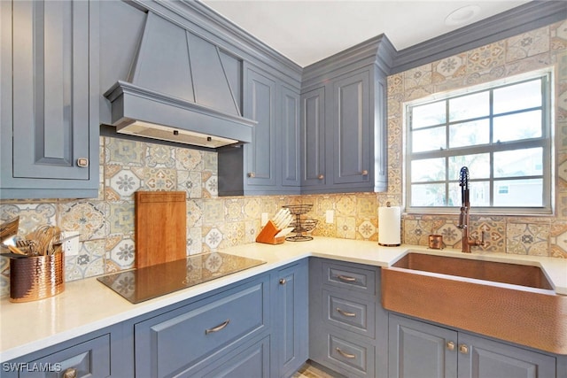 kitchen featuring black electric stovetop, decorative backsplash, premium range hood, and sink