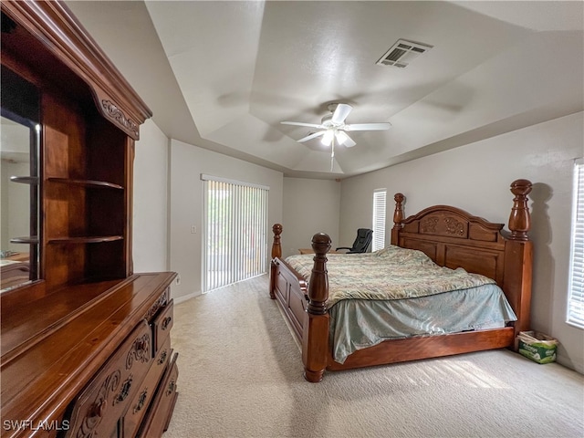 bedroom with ceiling fan, a tray ceiling, and light colored carpet