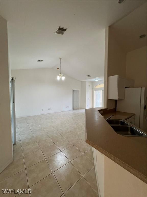 4895 Golfview Blvd, Lehigh Acres, FL 33973 - kitchen with lofted ceiling, freestanding refrigerator, dark countertops, white cabinets, and light tile patterned flooring