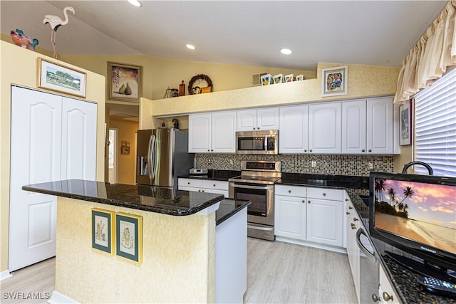 kitchen with appliances with stainless steel finishes, vaulted ceiling, a kitchen island, and white cabinets