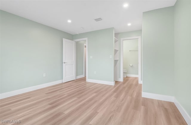 unfurnished bedroom featuring a closet, a walk in closet, light hardwood / wood-style floors, and ensuite bath