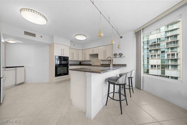 kitchen featuring pendant lighting, a kitchen breakfast bar, light tile patterned floors, double oven, and kitchen peninsula