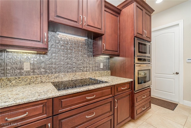 kitchen with light tile patterned flooring, under cabinet range hood, stainless steel appliances, backsplash, and light stone countertops