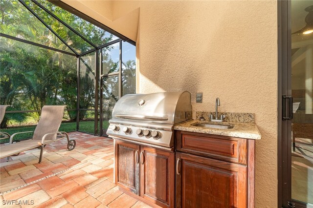 view of patio with glass enclosure, a sink, an outdoor kitchen, and area for grilling