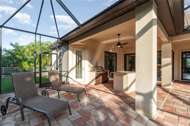 view of patio / terrace with a ceiling fan, glass enclosure, grilling area, fence, and exterior kitchen