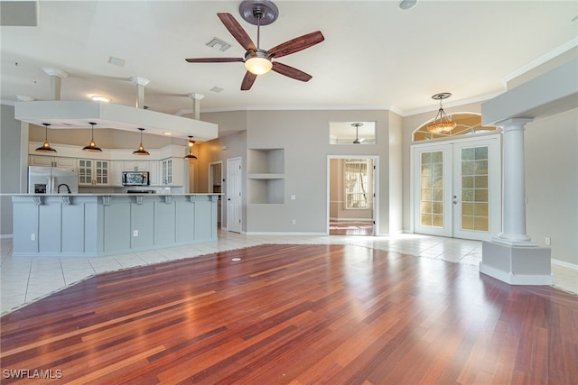 unfurnished living room featuring light wood-type flooring, french doors, decorative columns, ceiling fan, and built in shelves