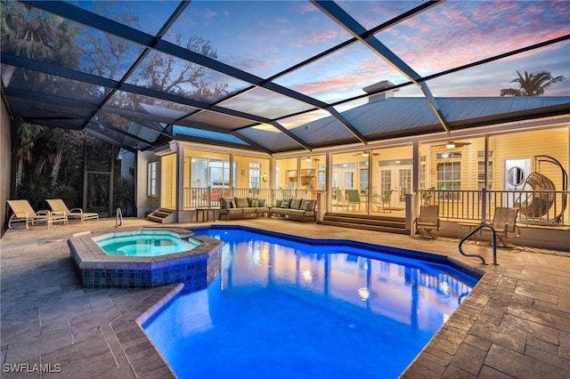 pool at dusk featuring an in ground hot tub, a patio area, glass enclosure, and ceiling fan