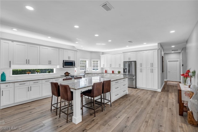 kitchen featuring light hardwood / wood-style floors, stainless steel appliances, a center island, and white cabinets