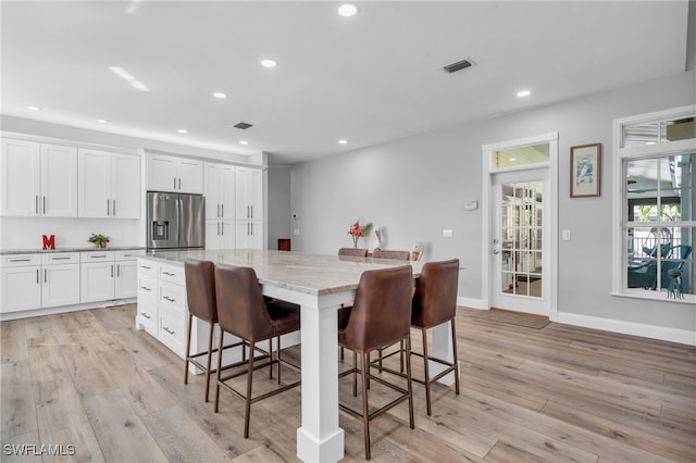 kitchen with a center island, stainless steel refrigerator with ice dispenser, light hardwood / wood-style flooring, and white cabinetry