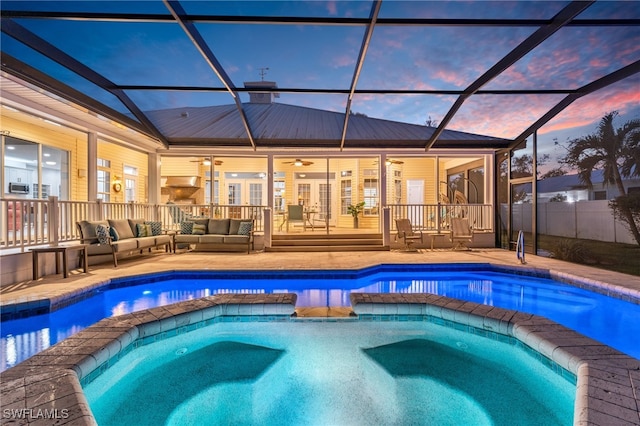 pool at dusk featuring a hot tub, an outdoor hangout area, ceiling fan, and a lanai