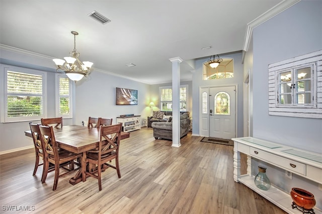 dining room featuring ornate columns, light hardwood / wood-style floors, crown molding, and an inviting chandelier