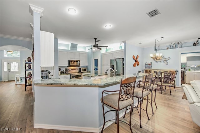 kitchen with kitchen peninsula, ornamental molding, light wood-type flooring, appliances with stainless steel finishes, and ceiling fan with notable chandelier