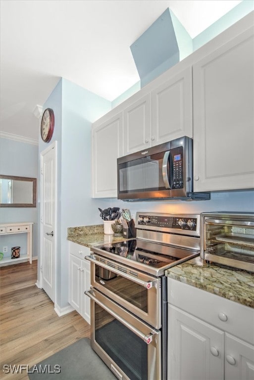 kitchen featuring appliances with stainless steel finishes, white cabinetry, stone counters, and light wood-type flooring