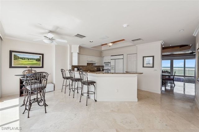 kitchen with backsplash, kitchen peninsula, crown molding, white appliances, and white cabinets