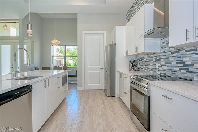 kitchen with sink, appliances with stainless steel finishes, wall chimney range hood, and white cabinetry