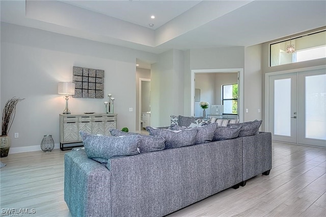 living room with french doors, a tray ceiling, and light wood-type flooring