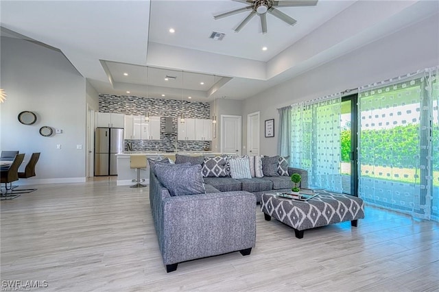 living room with light hardwood / wood-style floors, a tray ceiling, and ceiling fan