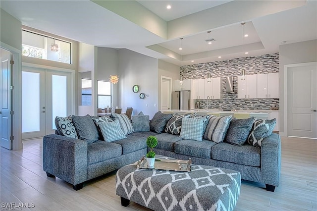 living room featuring a towering ceiling, french doors, light wood-type flooring, and a raised ceiling